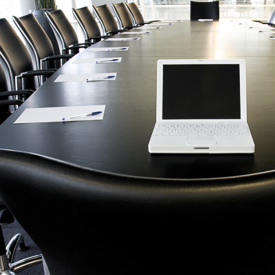 A laptop sits on a boardroom table set up for a business meeting.