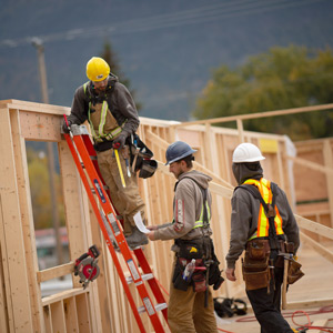 Construction worker on a ladder working with two other carpenters doing framing for a building in Nelson BC